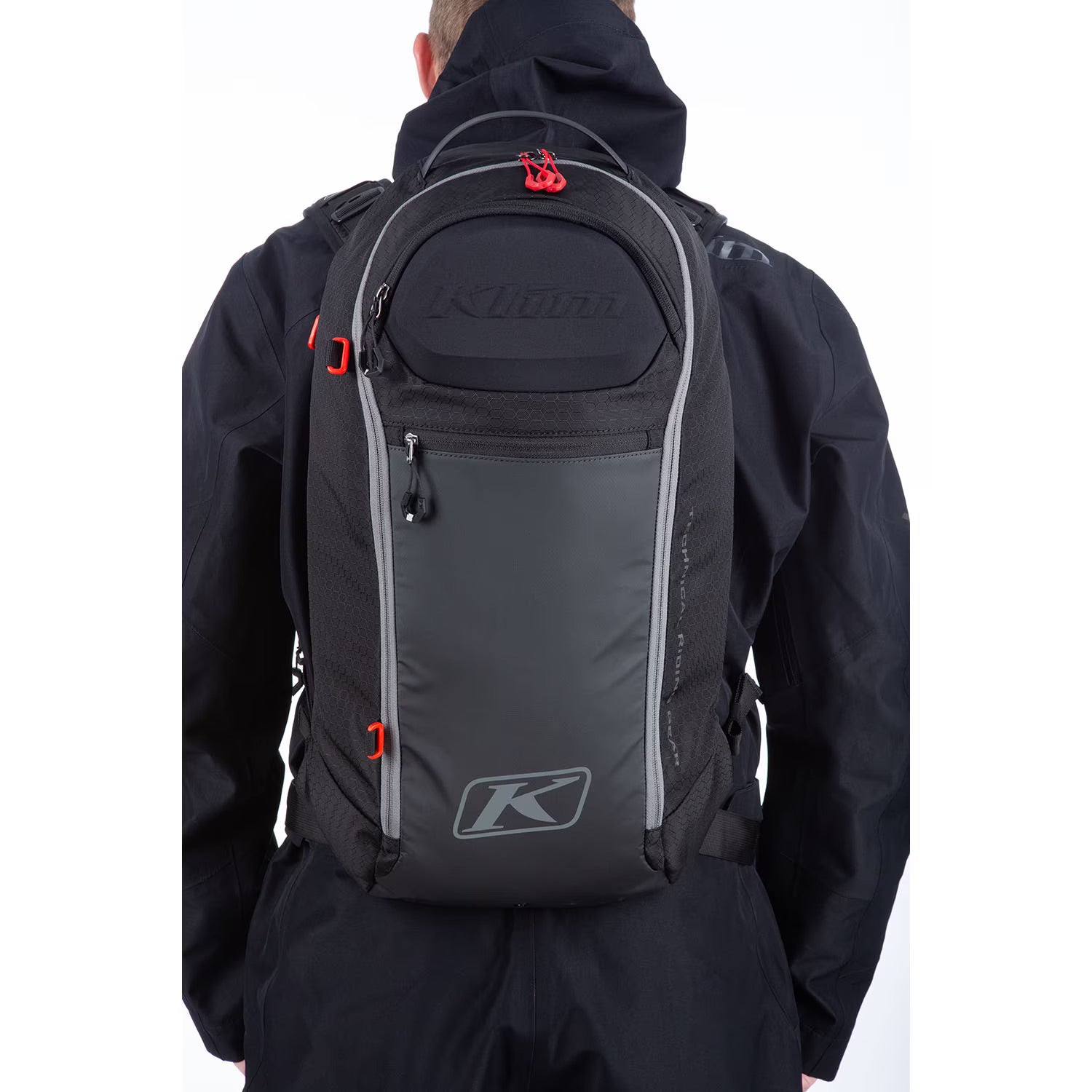 Person wearing a black jacket with a gray backpack featuring a brand logo on a white background
