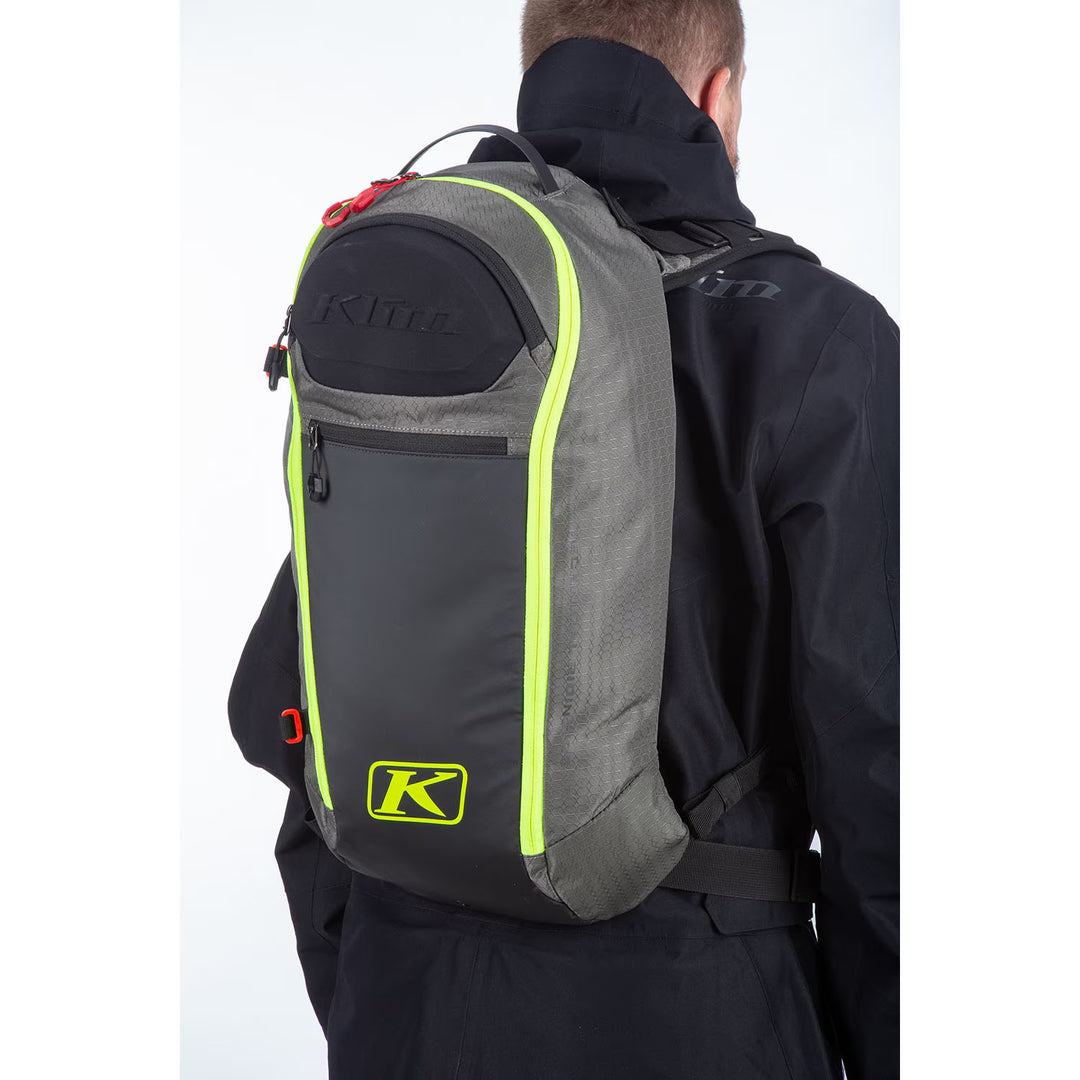 Person wearing a gray backpack with green accents and Klim logo on a white background