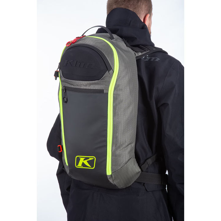 Person wearing a gray backpack with green accents and Klim logo on a white background