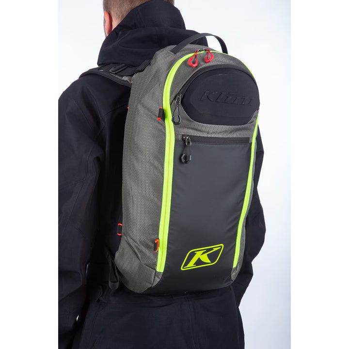 Person wearing a gray backpack with neon green accents and Klim logo on a white background