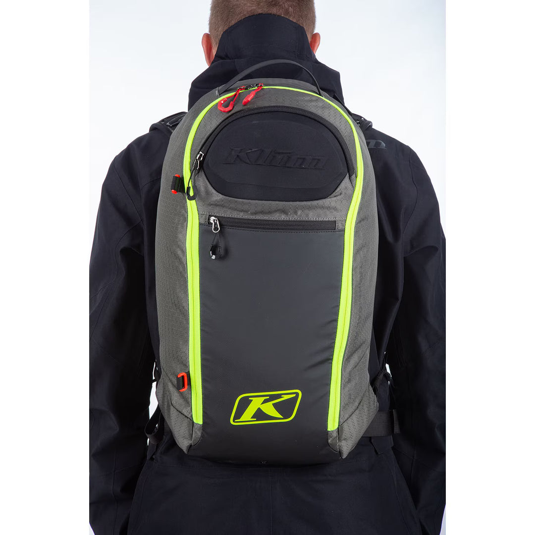 Person wearing a gray backpack with neon green accents and Klim logo on a white background