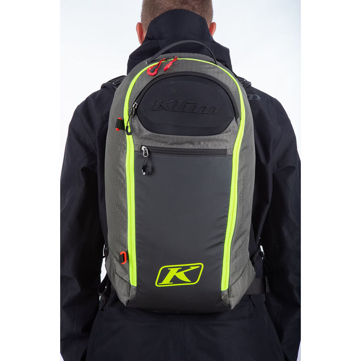 Person wearing a gray backpack with neon green accents and Klim logo on a white background