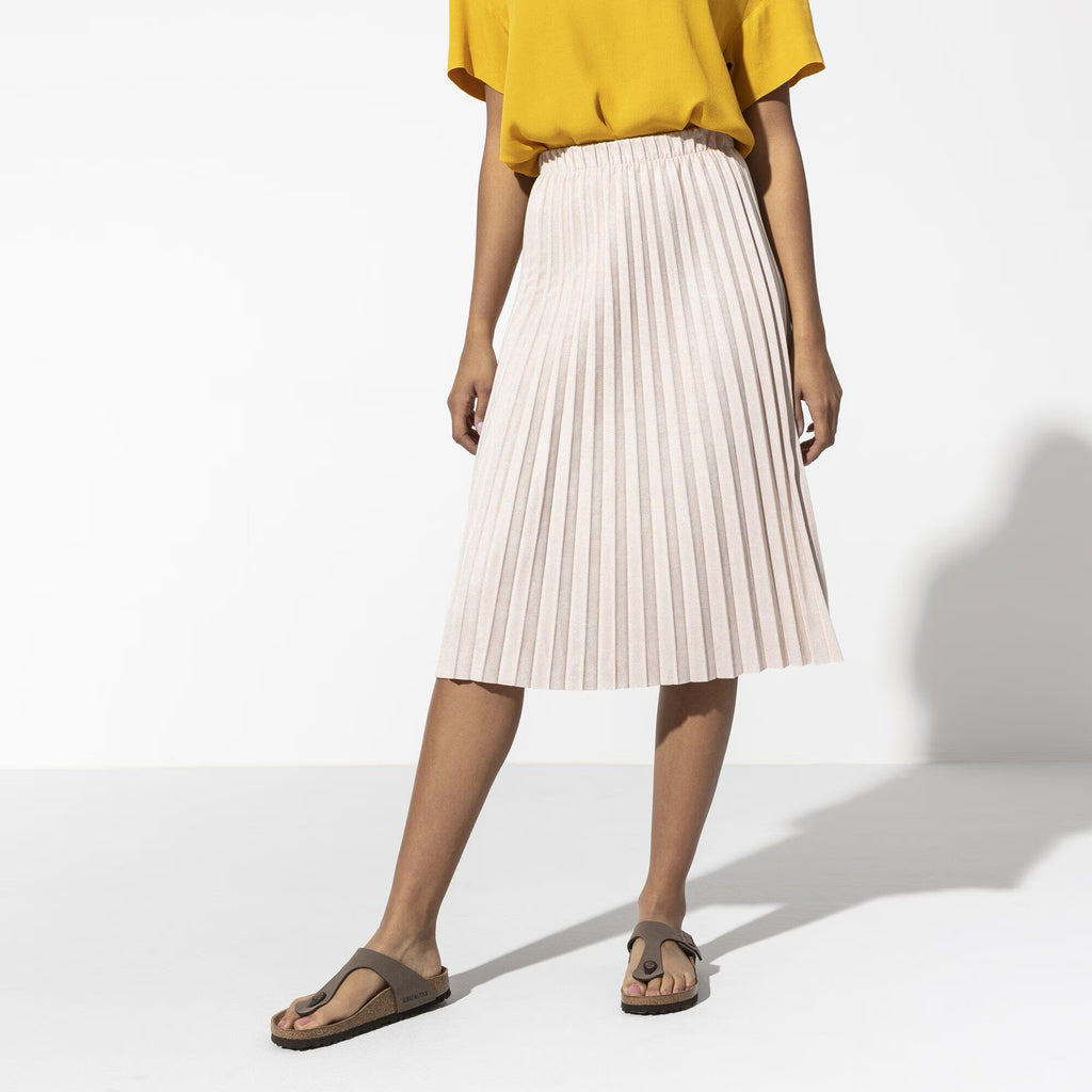 Person wearing a yellow top and white pleated skirt on a white background
