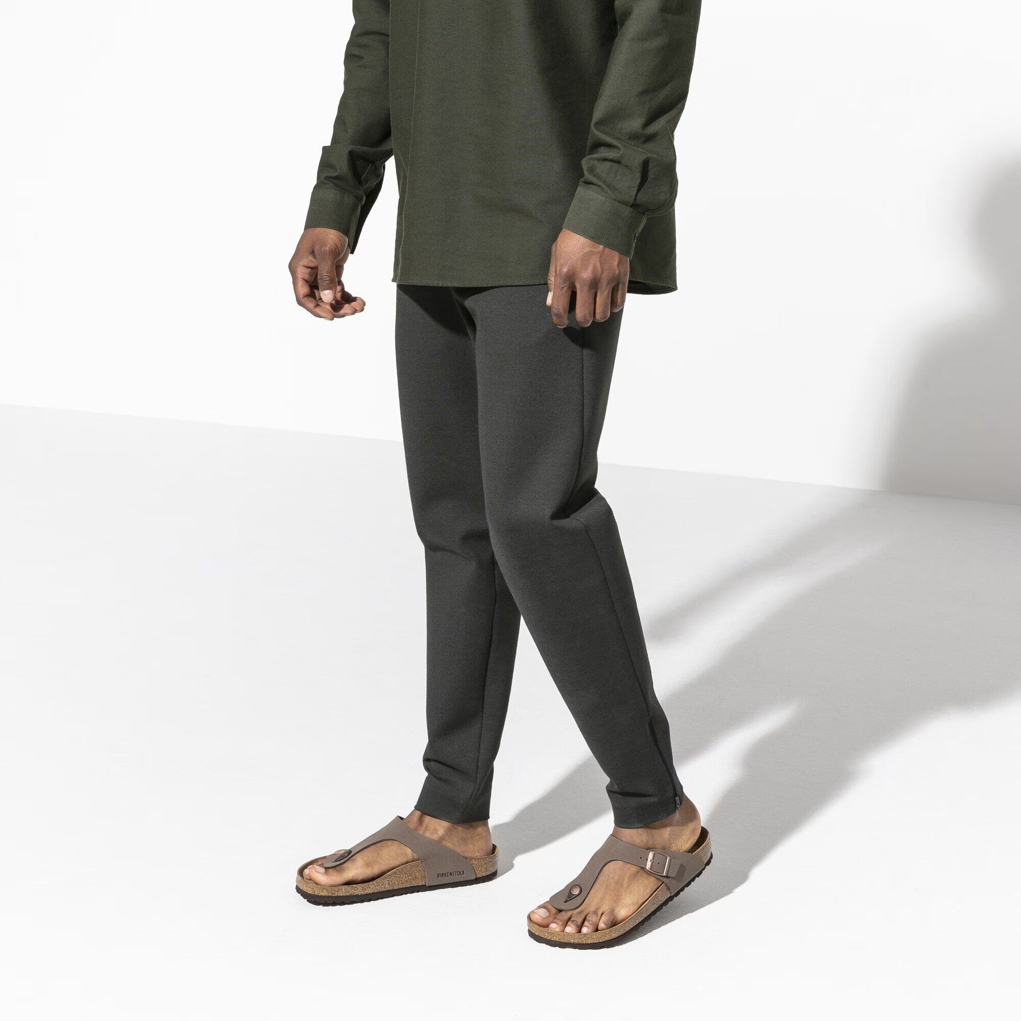Person wearing a green shirt and dark gray pants on a white background