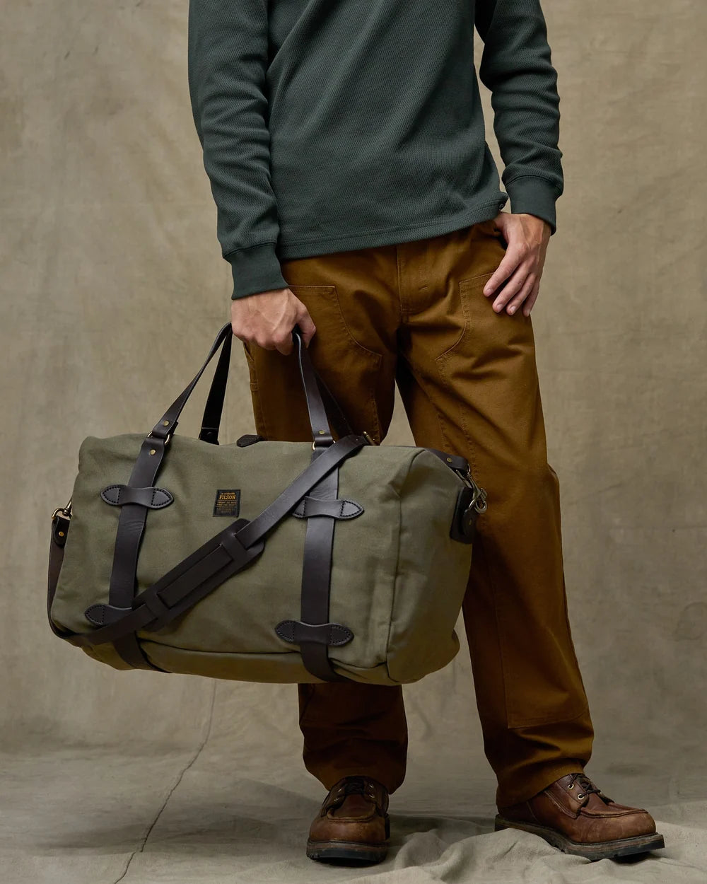 Person holding a green leather bag against a beige background