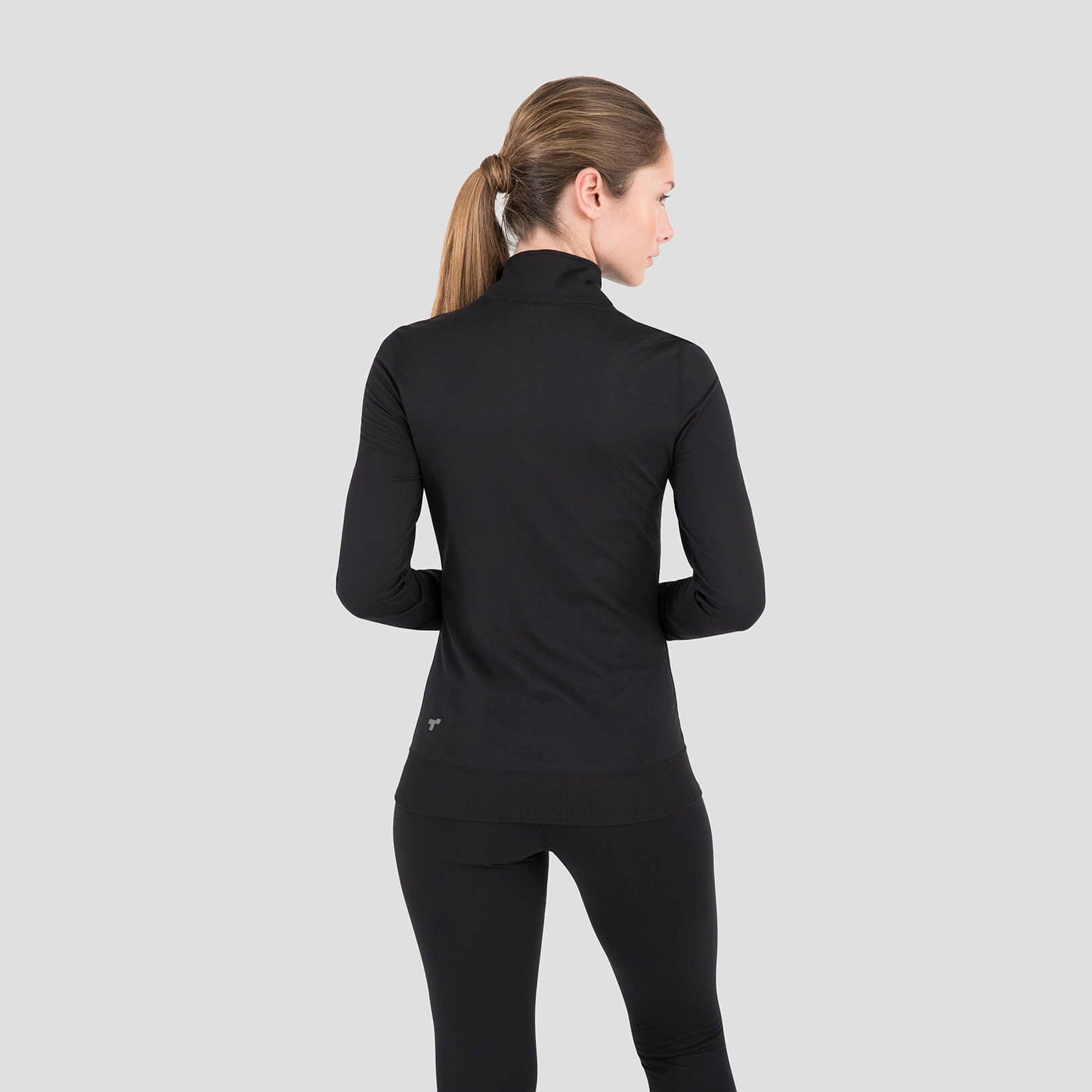 Woman wearing a black long-sleeve athletic top and leggings on a light gray background