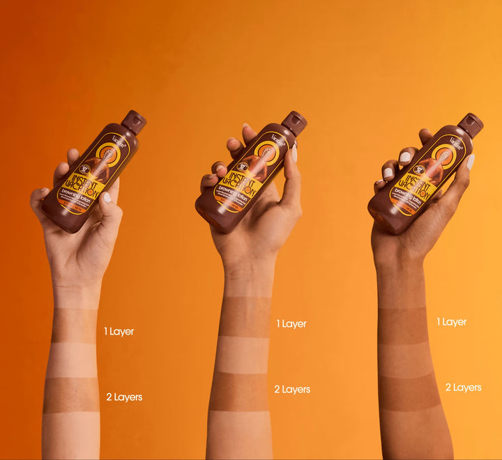 Three hands holding bottles of a hair product with different layers applied on an orange background.