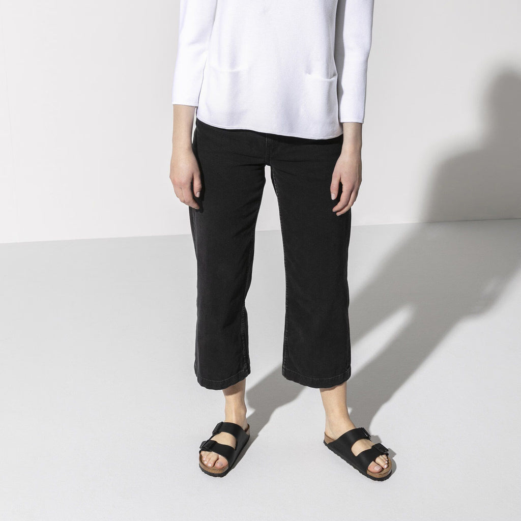 Person wearing a white shirt and black pants standing on a light gray background