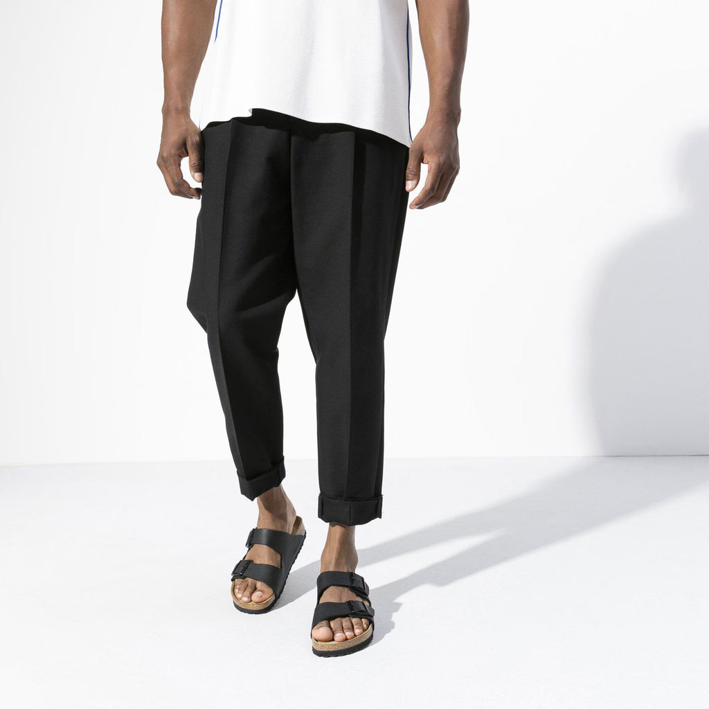 Person wearing black pants and sandals on a white background