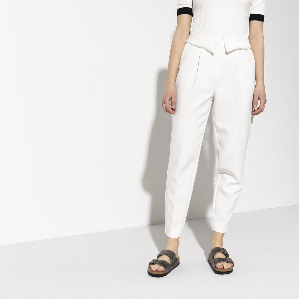 Person wearing white pants and a white top with black trim on a white background