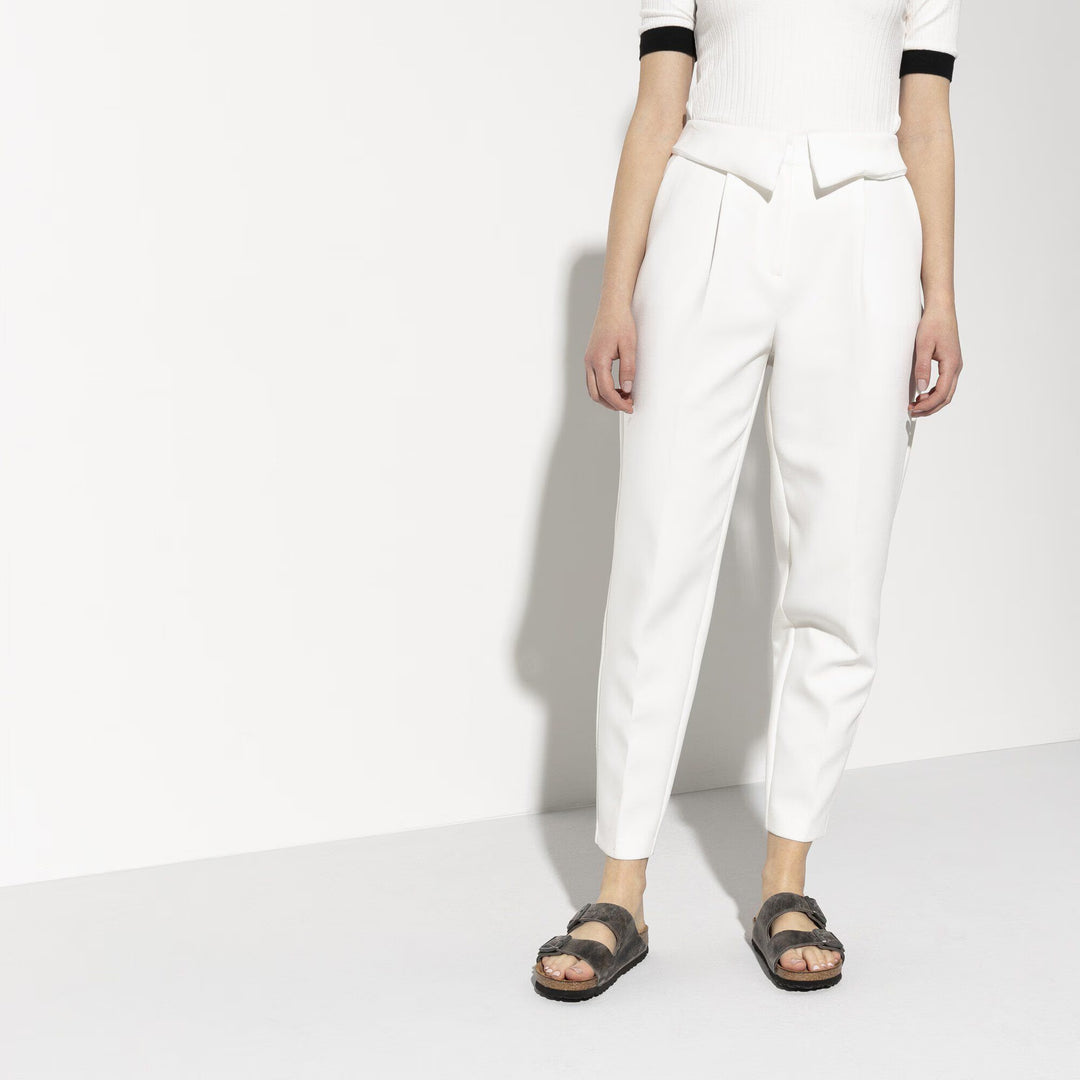 Person wearing white pants and a white top with black trim on a white background