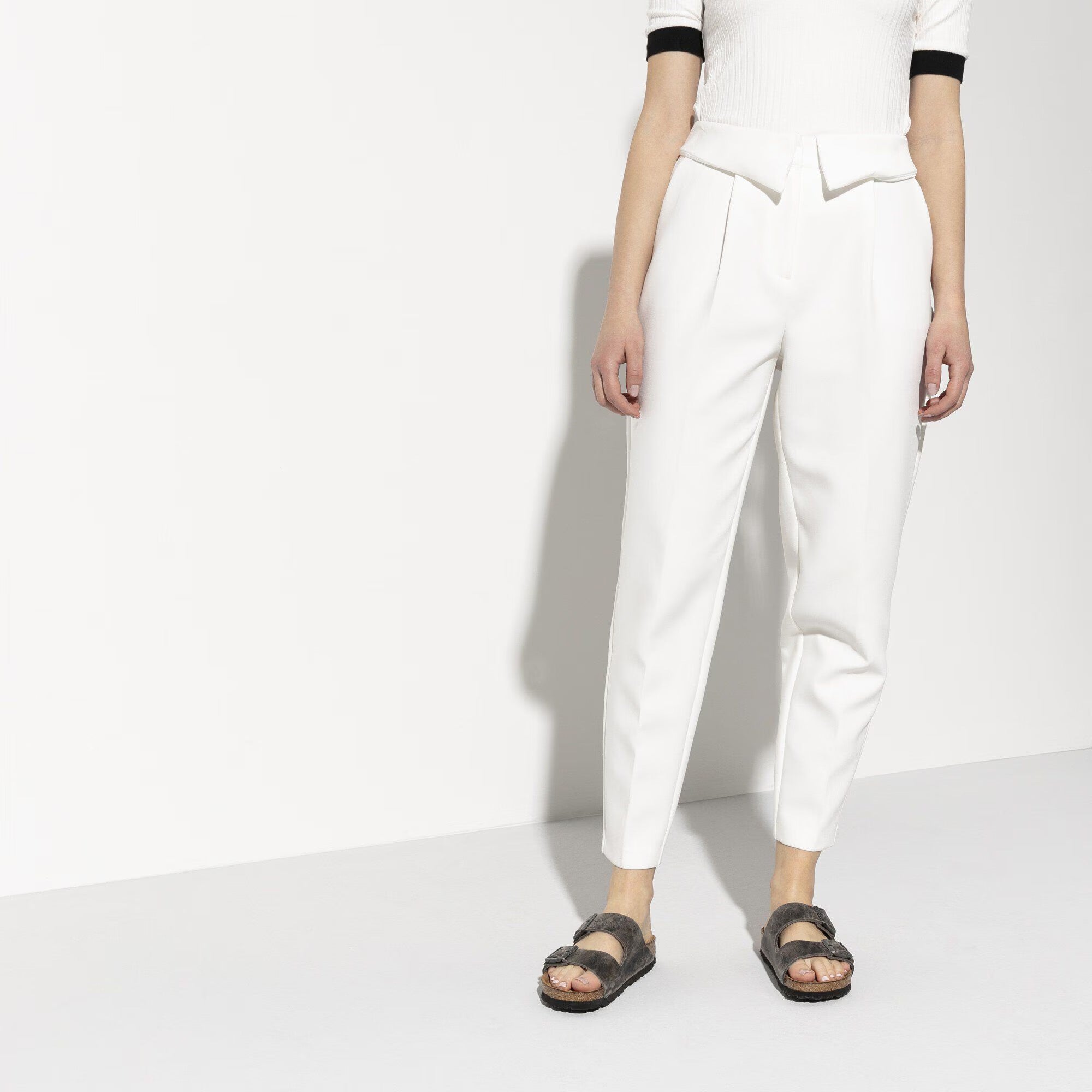 Person wearing white pants and a white top with black trim on a white background