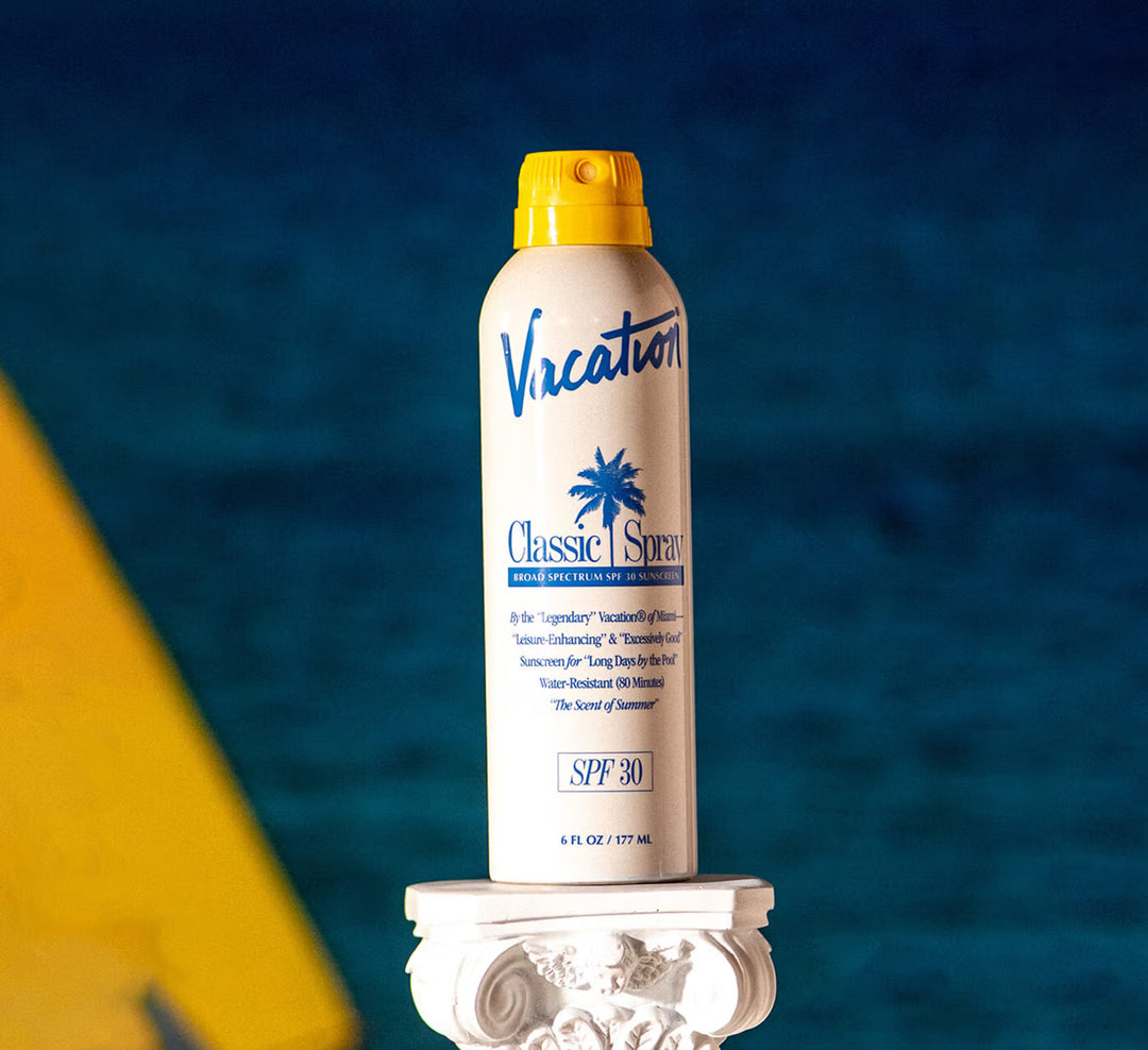 Sunspray bottle labeled 'Vacation Classic Spread' on a decorative pedestal with a blue background