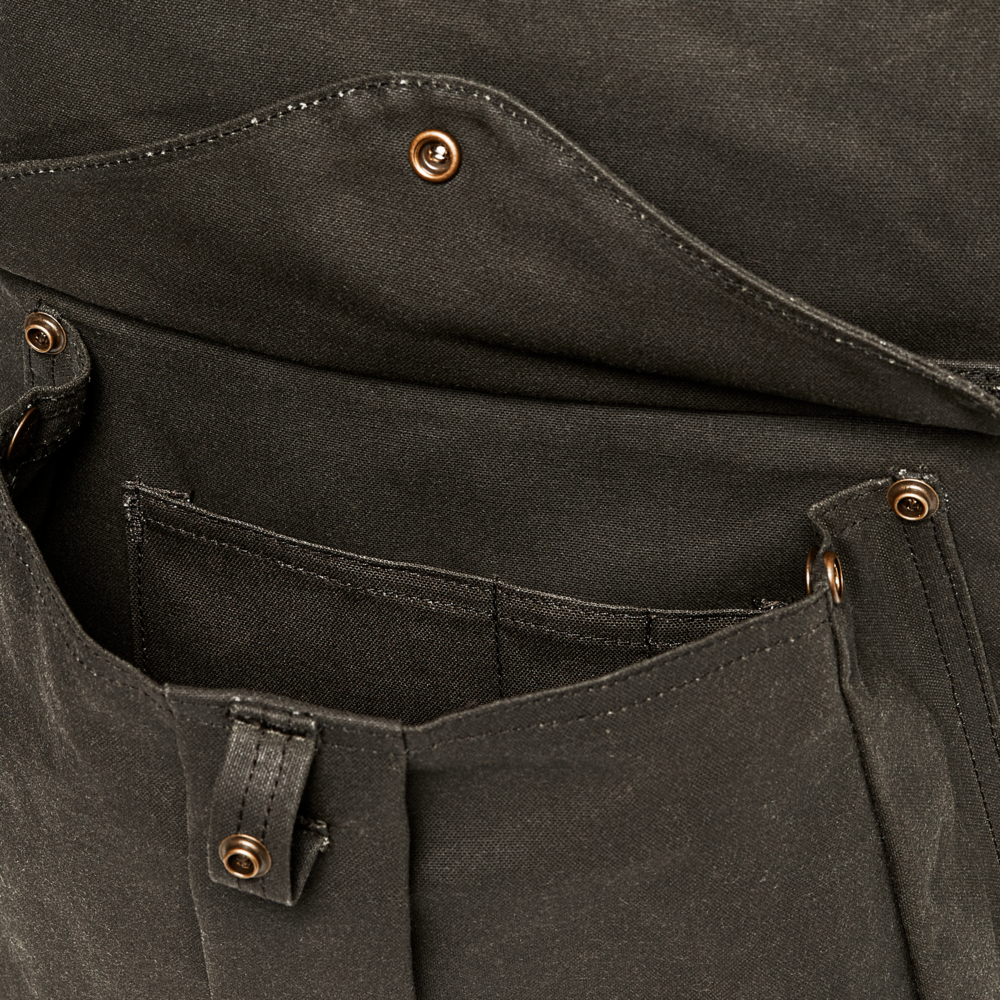 Close-up of a dark olive green canvas utility pocket with brass rivets and a metal zipper pull.