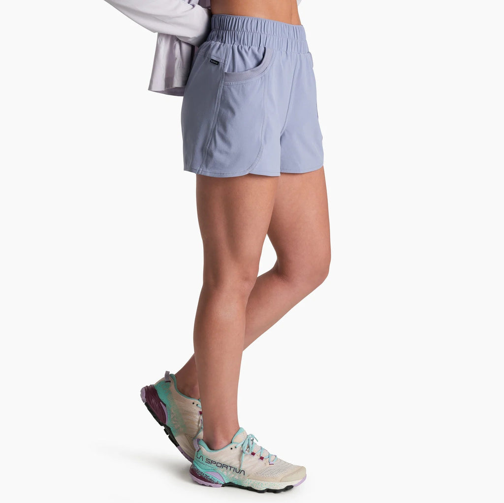A side view of a model wearing light blue athletic shorts, a white long-sleeve top, and running shoes against a plain white background.