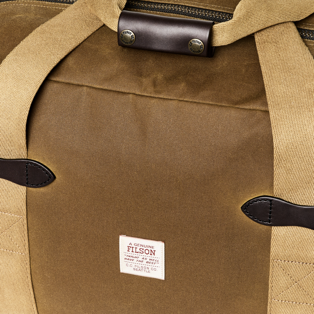 Close-up of a Filson duffel bag in tan waxed canvas with dark brown leather trim and a visible white Filson brand patch.
