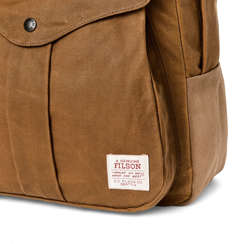 Close-up of a brown waxed canvas Filson bag showing a flap pocket with a snap button and the Filson brand label sewn onto the front.