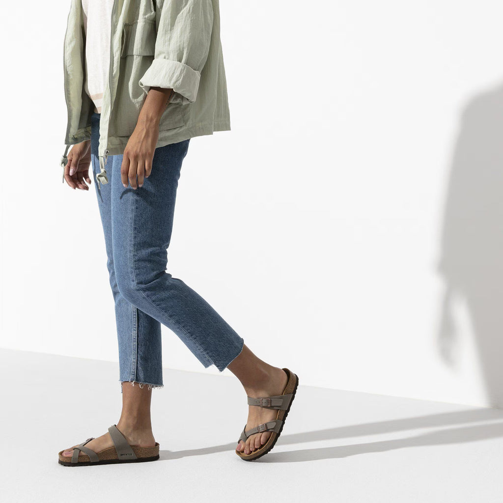 Person wearing blue jeans and brown sandals on a white background