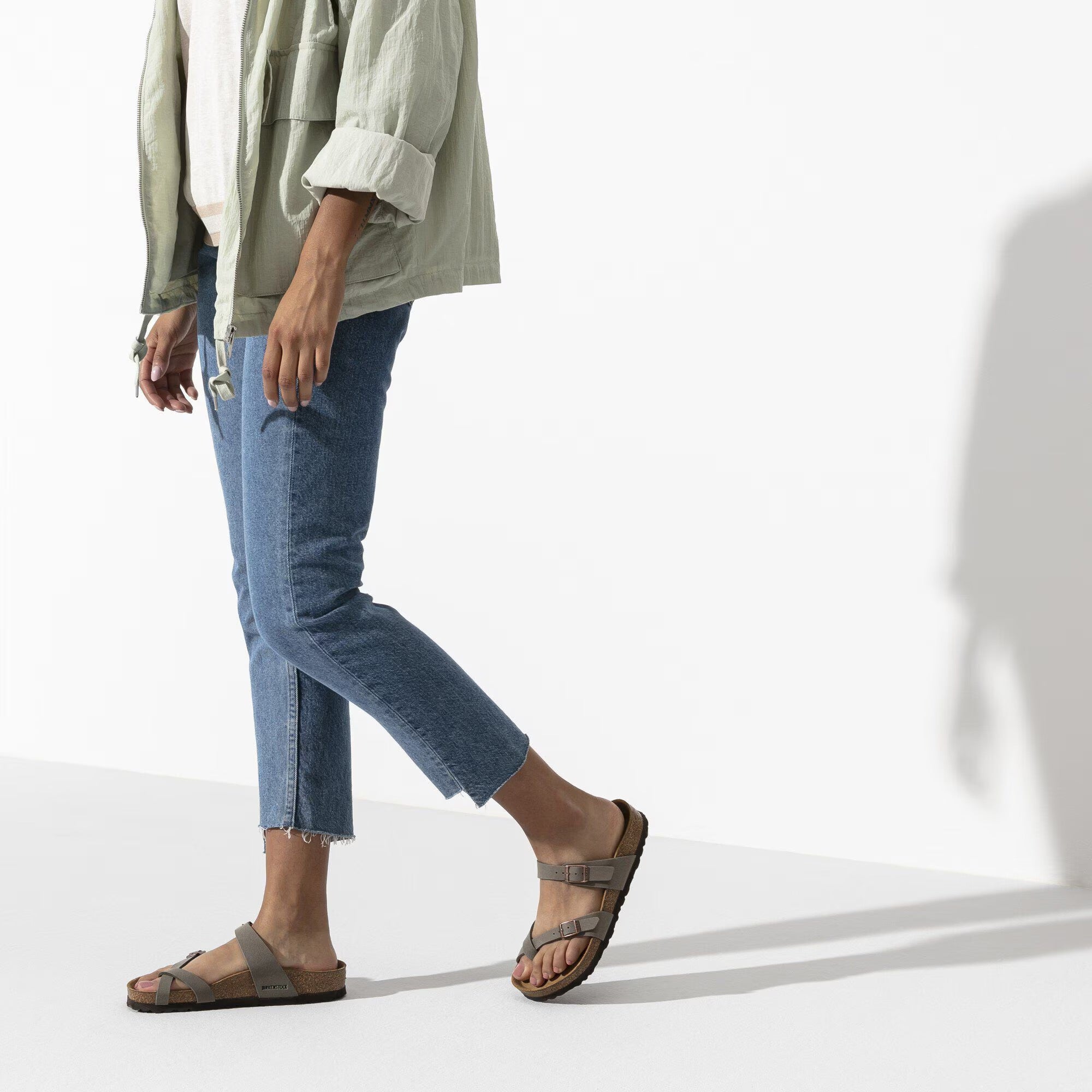 Person wearing blue jeans and brown sandals on a white background
