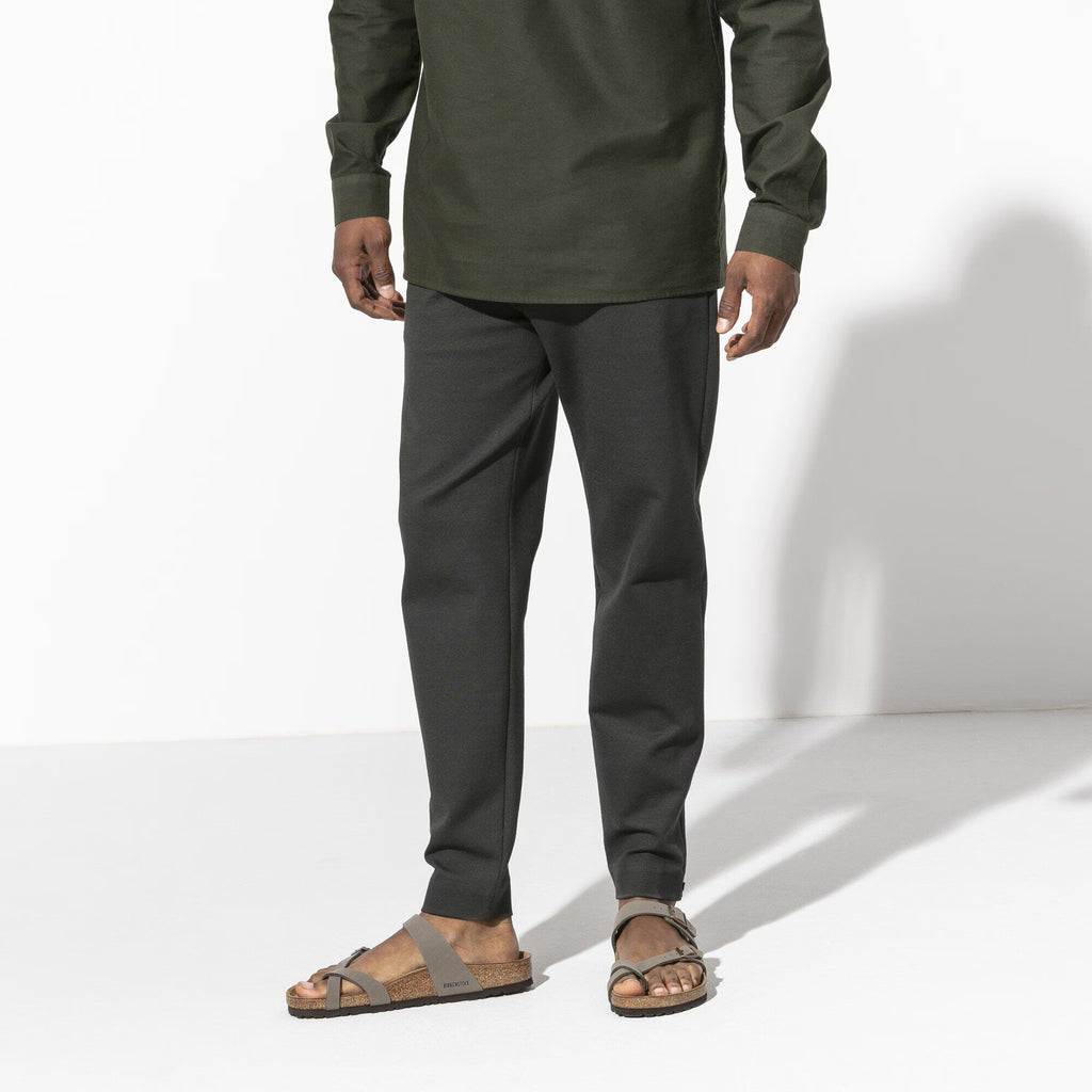 Person wearing a green shirt and gray pants on a white background