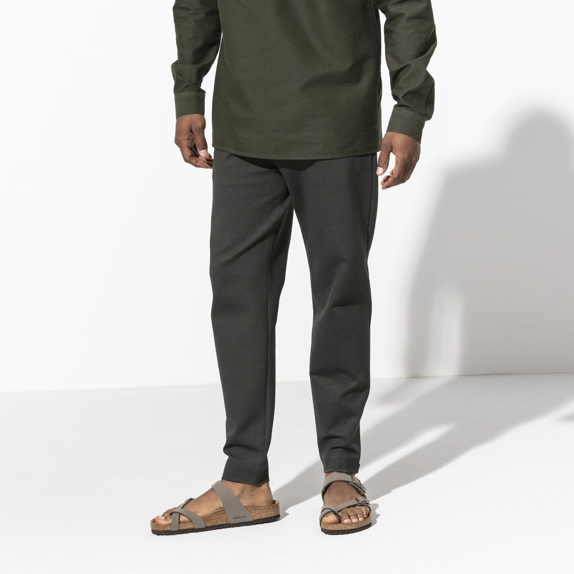 Person wearing a green shirt and gray pants on a white background