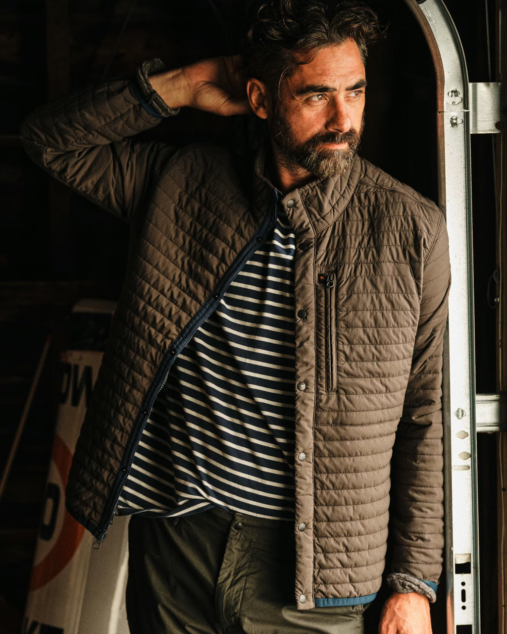 Man wearing a quilted jacket standing next to a vehicle with a dark background