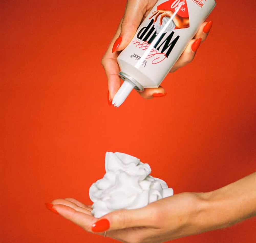 Person holding a can of whipped sunscreen against a red background