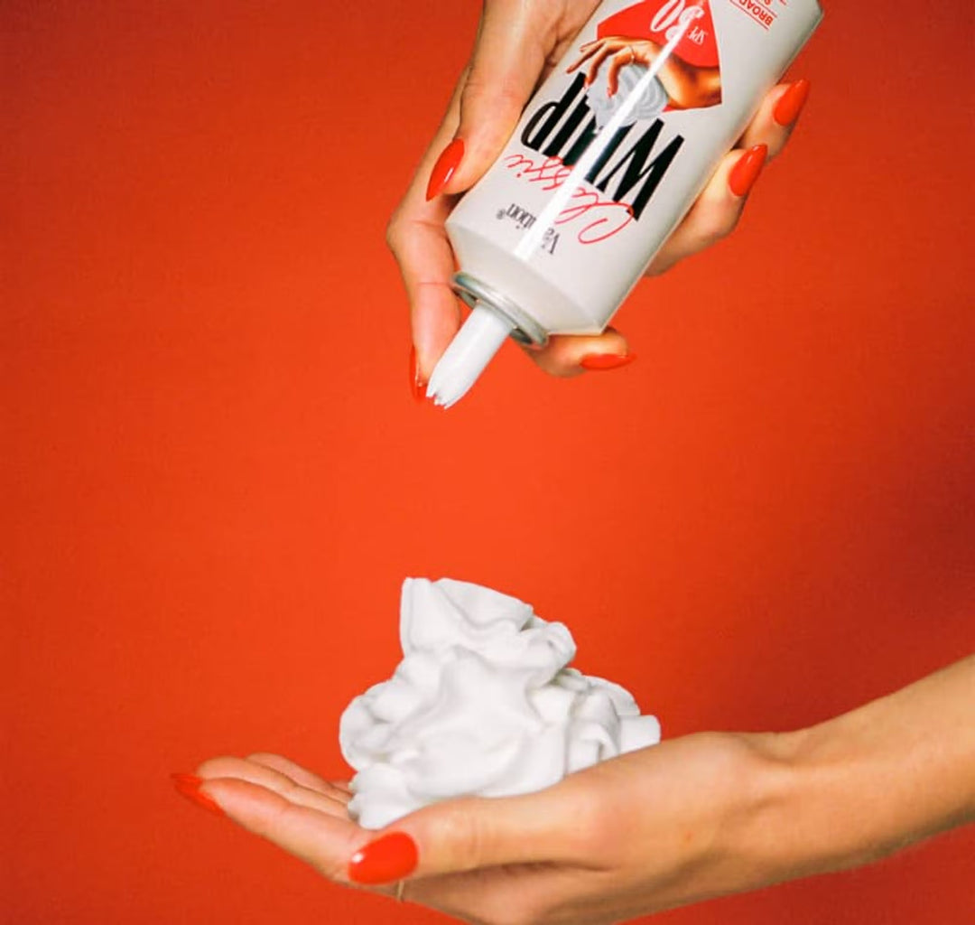 Person holding a can of whipped sunscreen against a red background