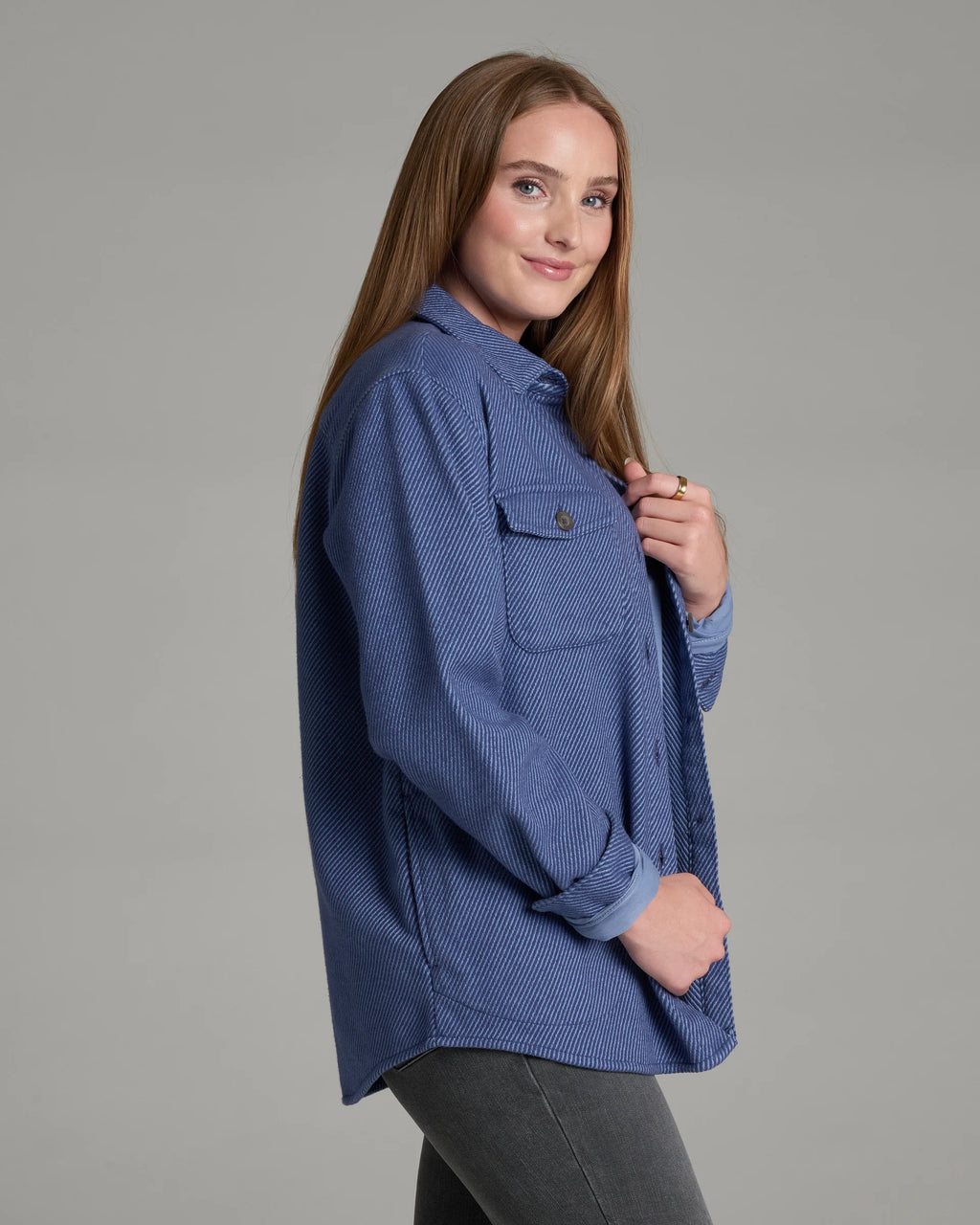 A woman modeling a blue textured button-up shirt with a chest pocket, photographed against a solid gray studio background.