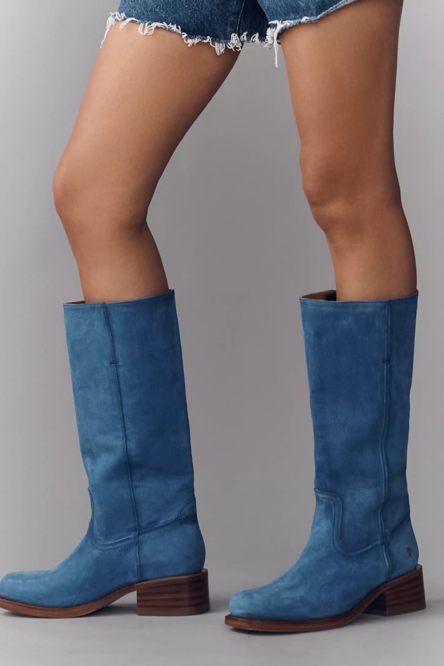Blue suede knee-high boots worn with denim shorts on a gray background