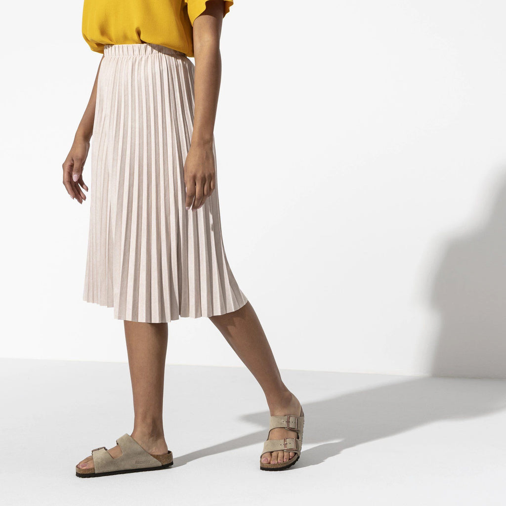 Person wearing a yellow top and beige pleated skirt on a white background