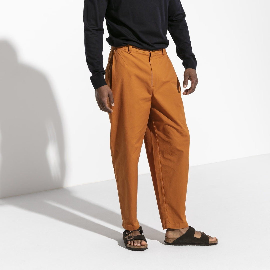 Person wearing orange pants and black shirt on a white background