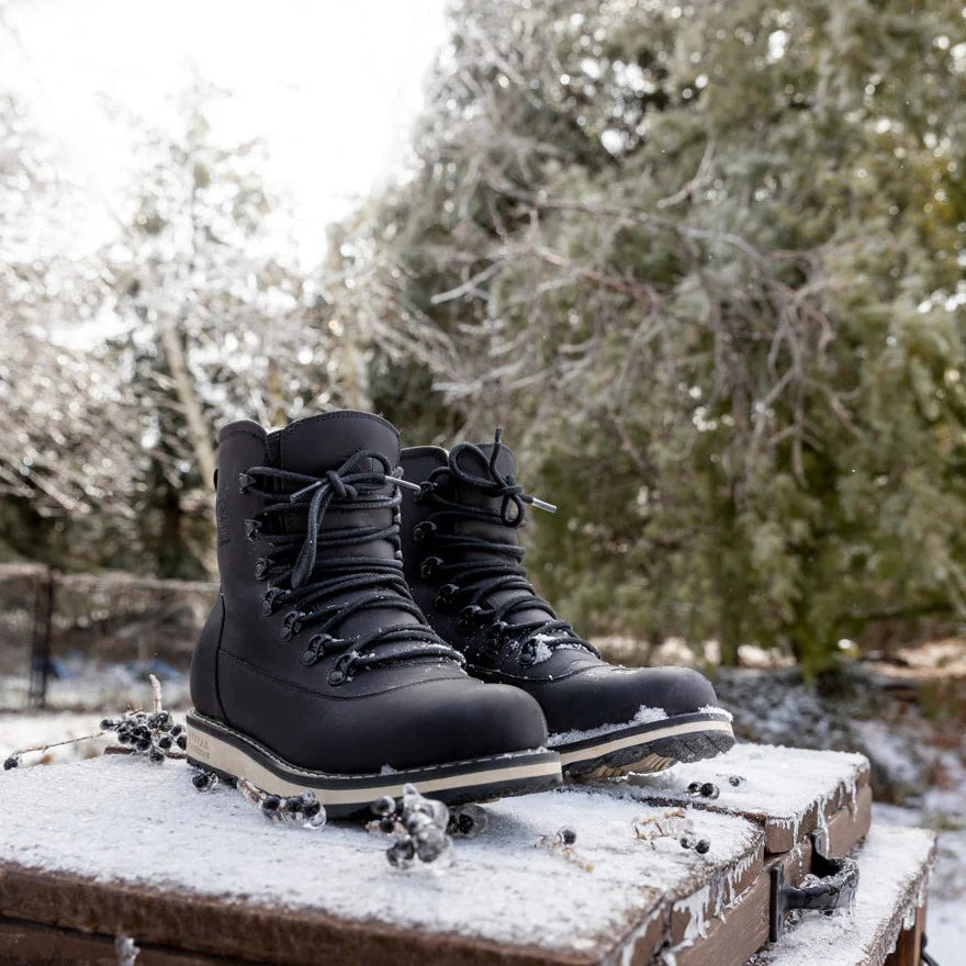 Black winter boots on a snowy surface with trees in the background