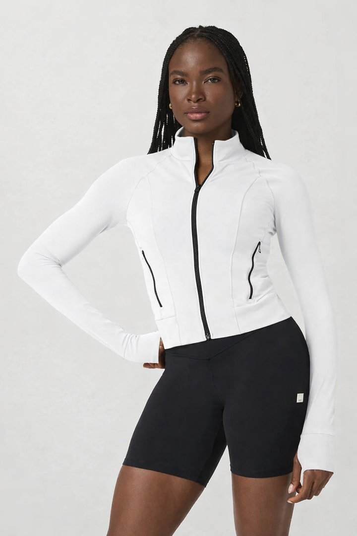 Woman wearing a white athletic jacket and black shorts on a light gray background