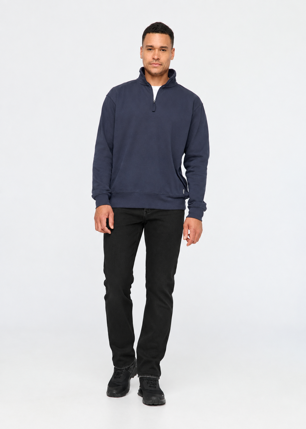A man modeling a navy blue quarter-zip sweatshirt with black pants and black shoes, standing against a plain white studio background.