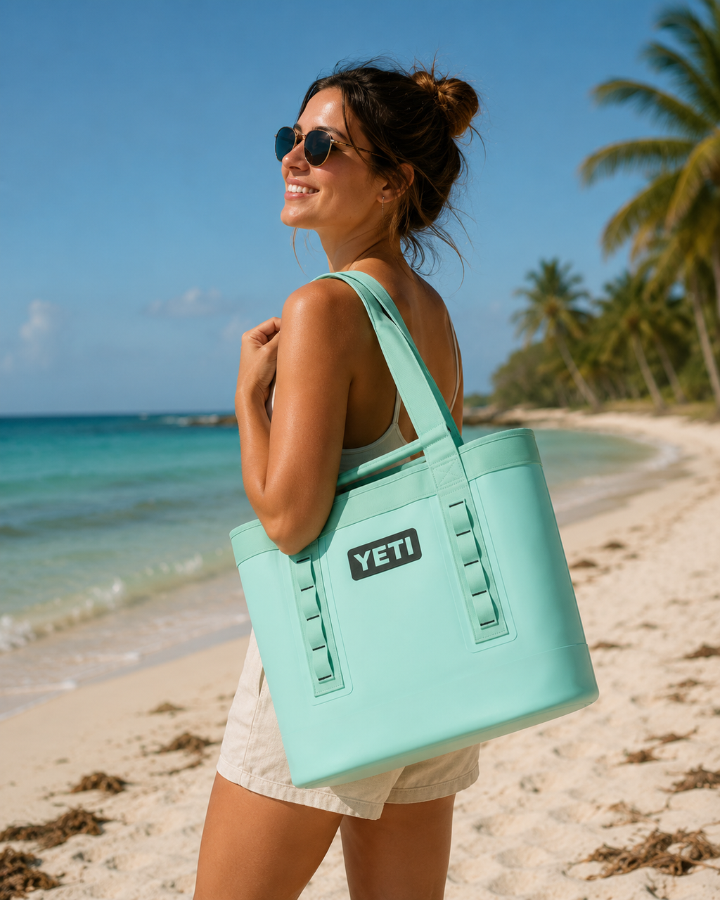 Woman holding a YETI cooler on a beach with palm trees and blue sky.