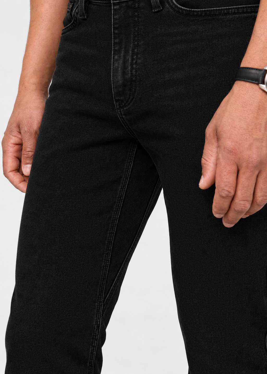 Close-up of a person wearing black denim jeans against a light gray studio background.