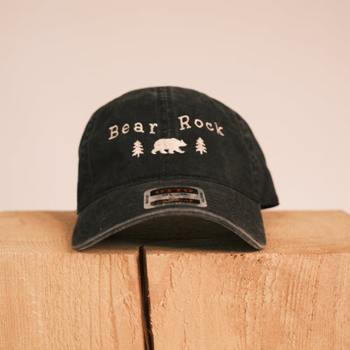 A black distressed baseball cap with 'Bear Rock' and a bear graphic embroidered on the front, displayed on a light wood block against a beige background.