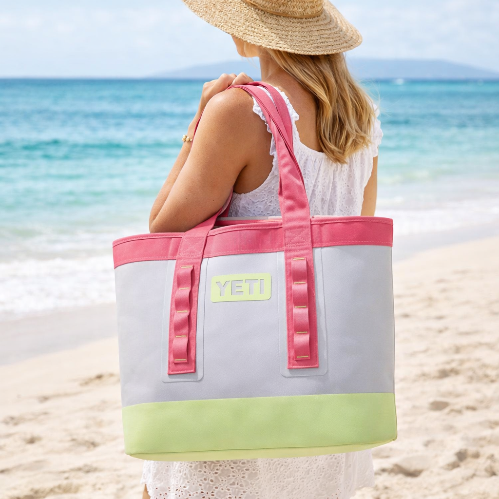 Woman holding a YETI branded beach bag on a sandy beach with ocean in the background
