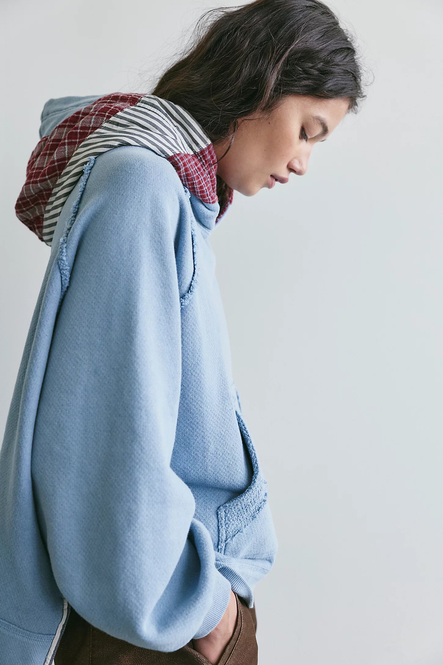 side view of woman modeling light blue hooded shirt with red plaid and black and white stripes on the hood, white background