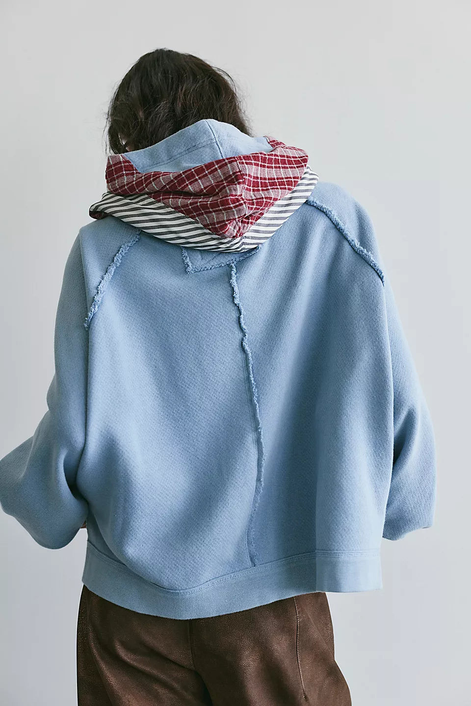 back view of woman modeling light blue hooded sweatshirt with red plaid and black and white stripes on hood. 
