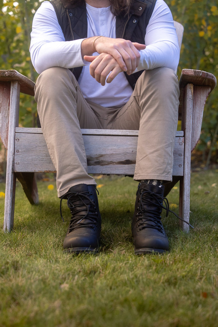 Person sitting on a wooden bench outdoors wearing beige pants and black boots.