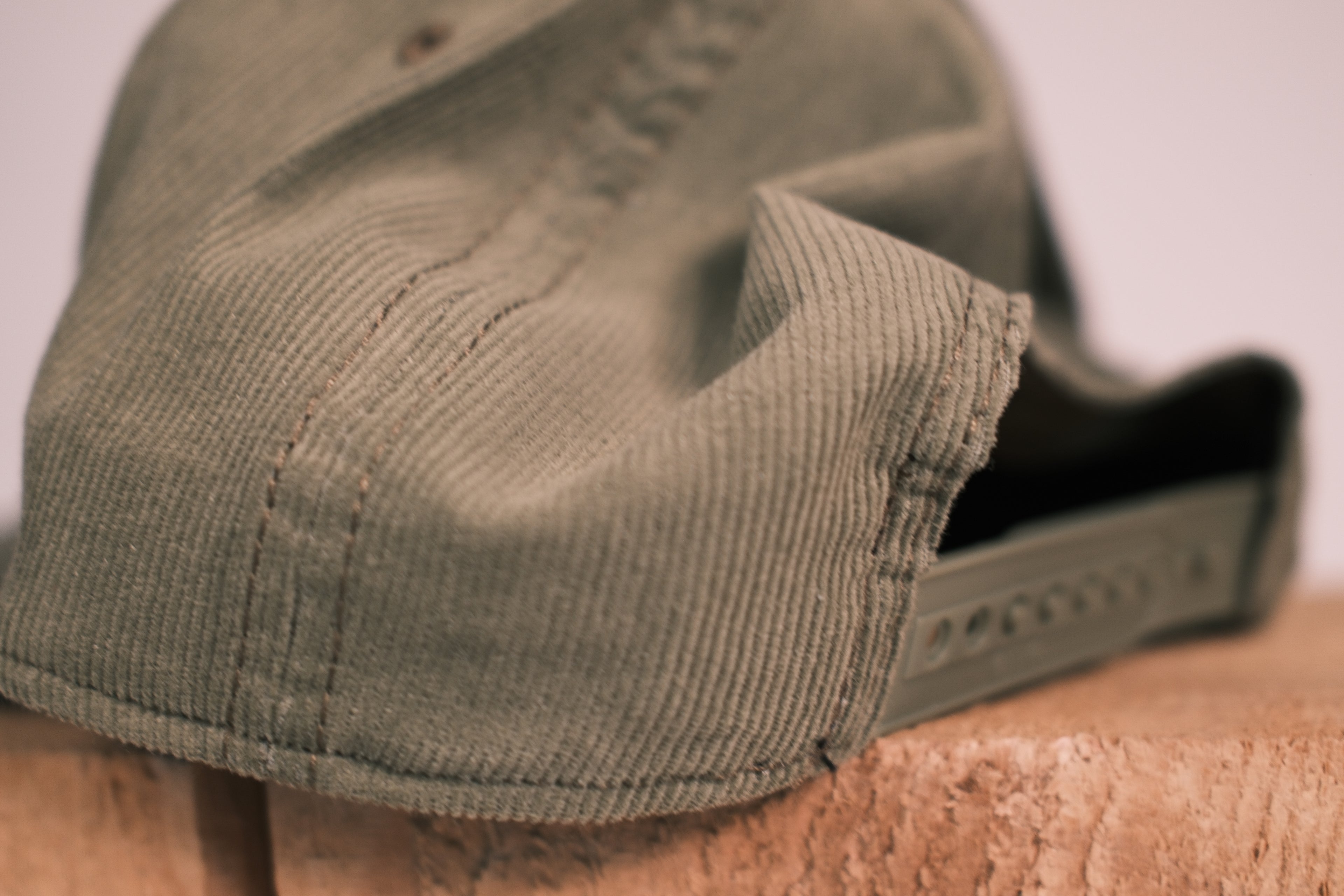 Close-up of the side and back of an olive green corduroy cap resting on a textured wooden surface.
