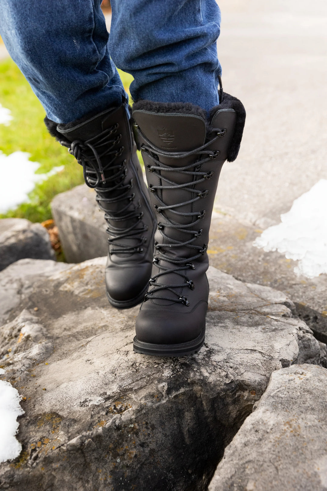 Black boots on a rocky surface with snow and grass in the background