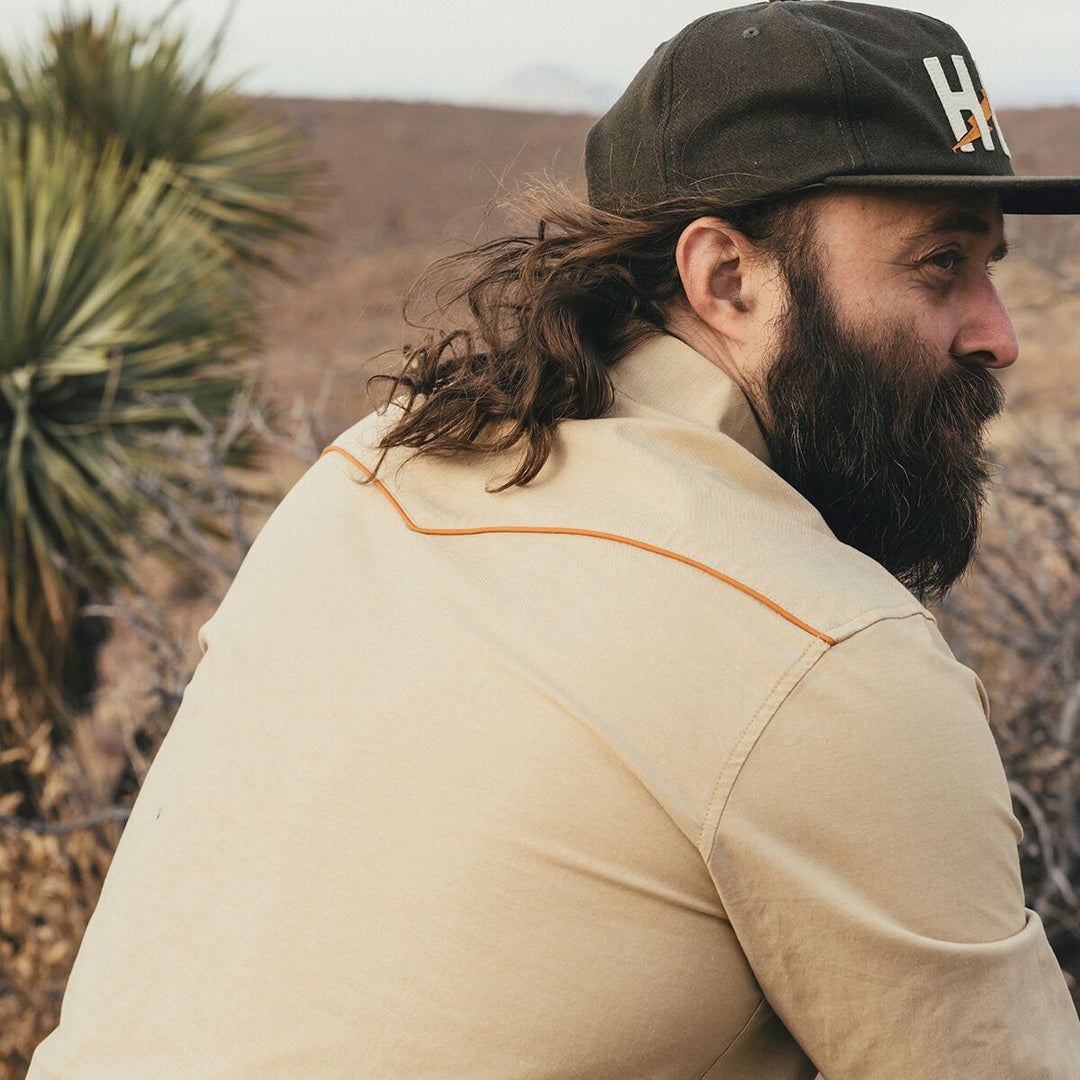 Man with a beard wearing a cap and beige shirt in a desert setting