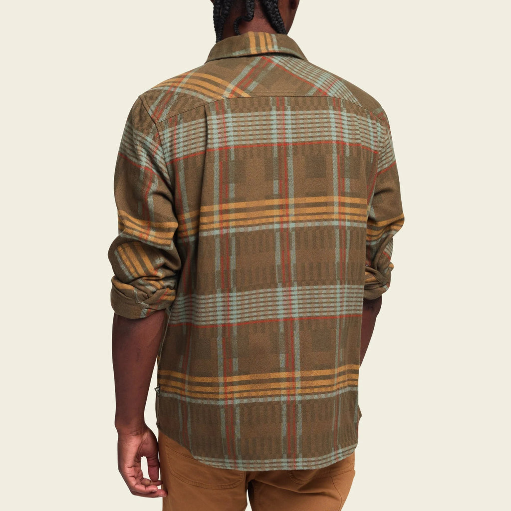 A long-sleeved plaid flannel shirt with a button-through flap pocket on the left chest, reinforced elbow patches, and custom metal buttons.