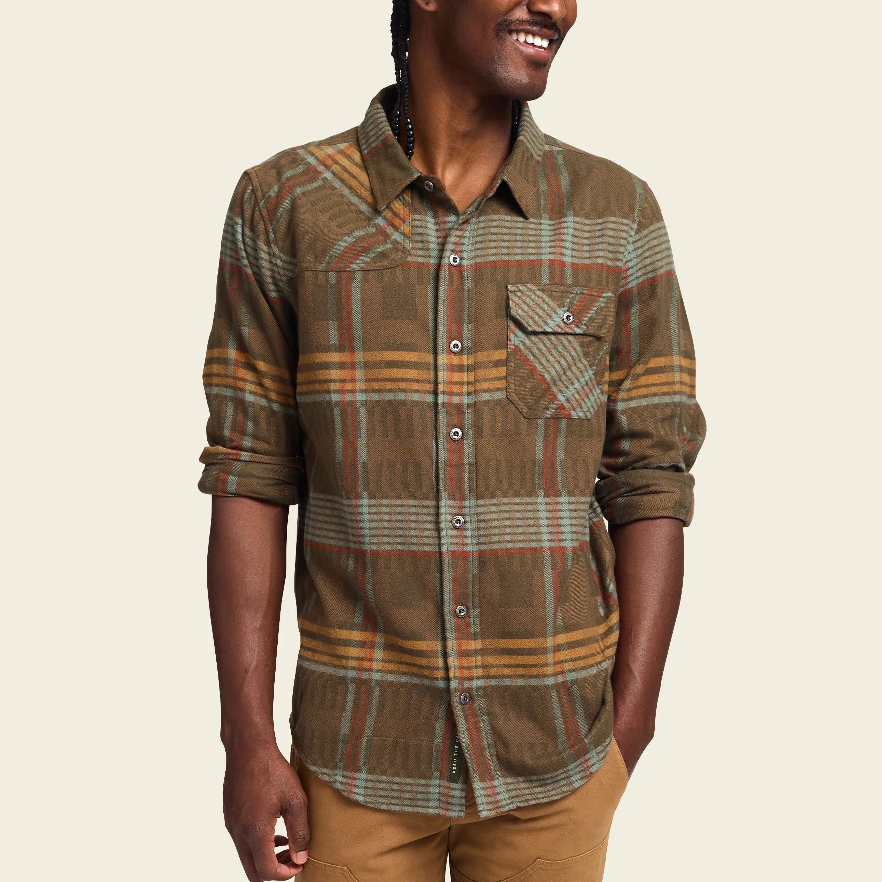 A long-sleeved plaid flannel shirt with a button-through flap pocket on the left chest, reinforced elbow patches, and custom metal buttons.