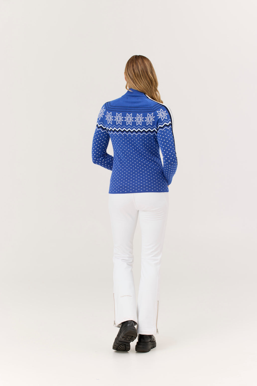 Woman wearing a blue patterned sweater and white pants on a light gray background