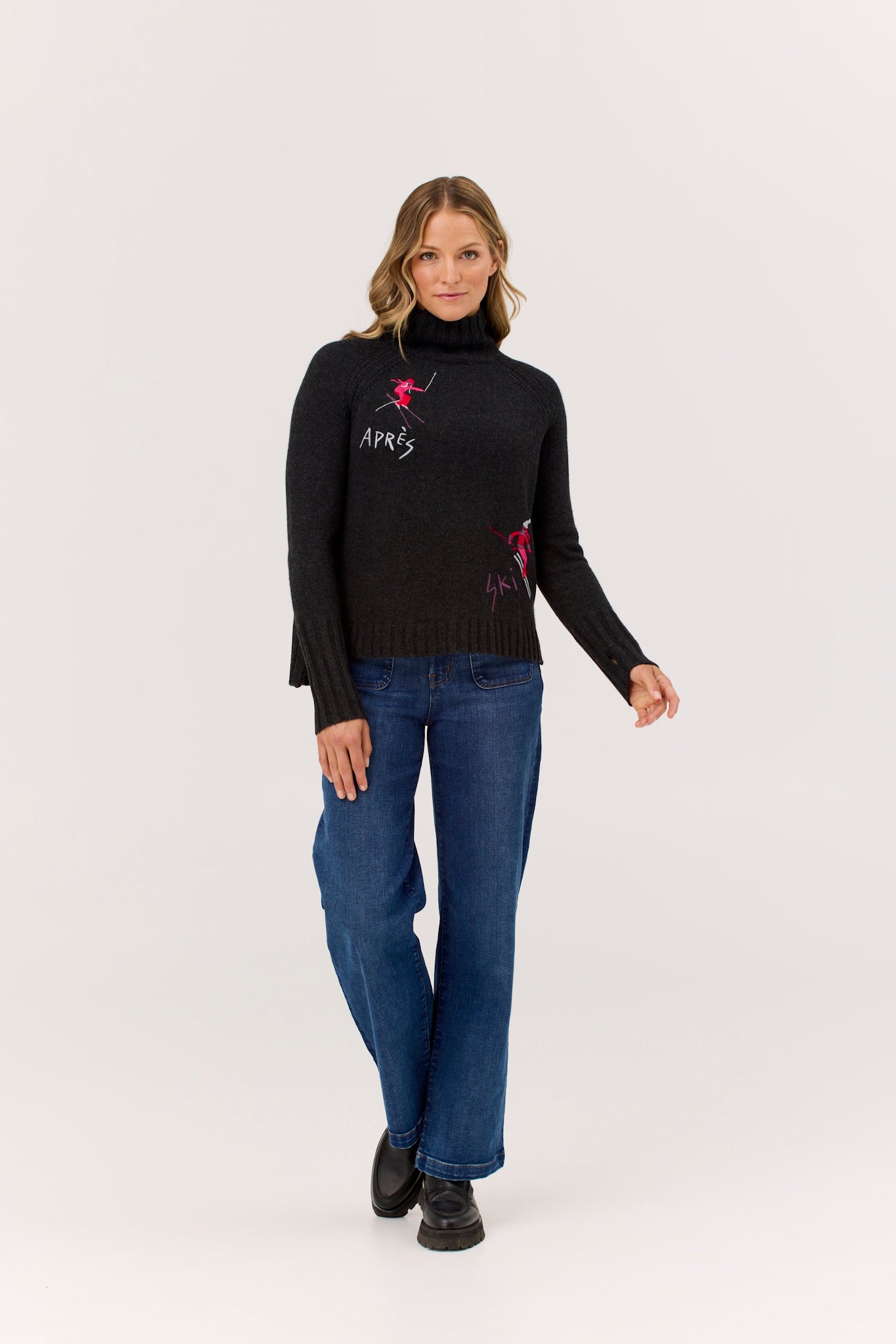 Woman wearing a black sweater with pink designs and blue jeans on a white background