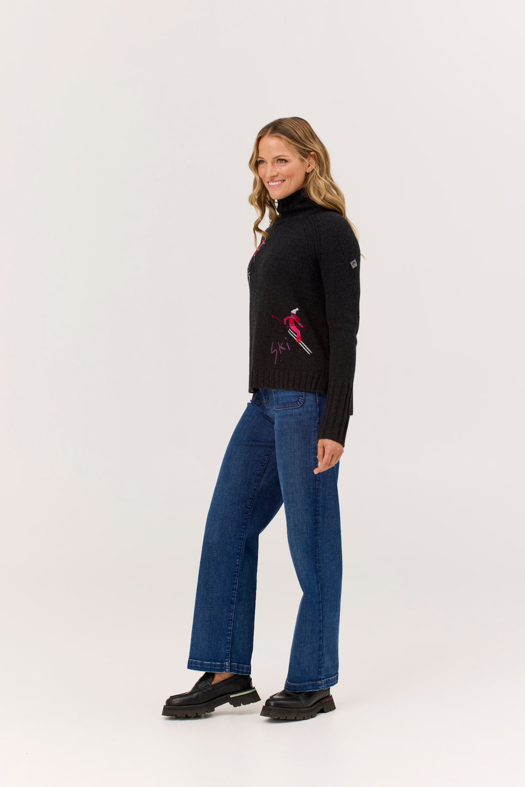 Woman wearing a black turtleneck with a red design and blue jeans on a white background